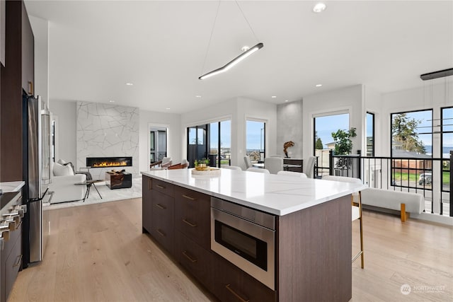 kitchen with appliances with stainless steel finishes, a kitchen breakfast bar, light hardwood / wood-style flooring, a premium fireplace, and a large island