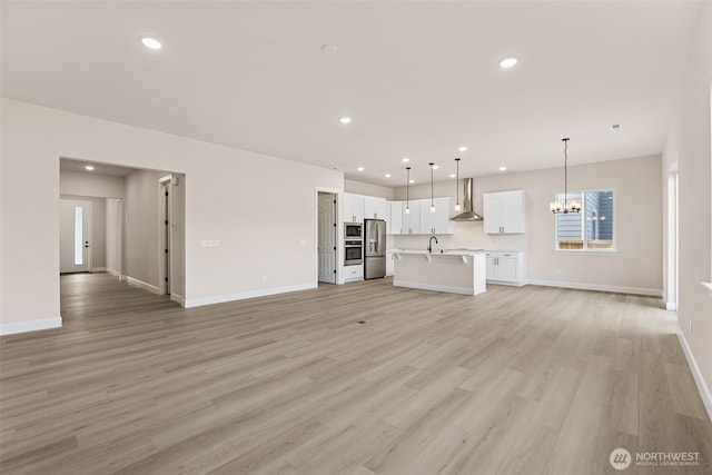 unfurnished living room featuring light wood-style flooring, baseboards, a sink, and recessed lighting