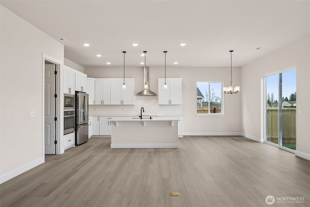 kitchen featuring stainless steel appliances, tasteful backsplash, light countertops, a sink, and wall chimney range hood