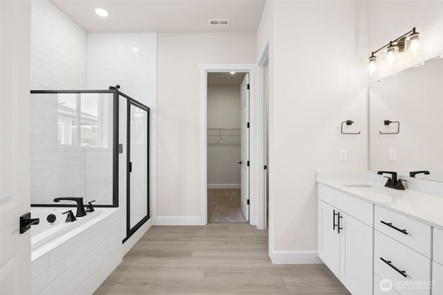 bathroom featuring a stall shower, a walk in closet, visible vents, and wood finished floors