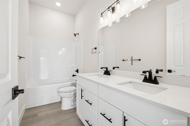 full bath with toilet, double vanity, a sink, and wood finished floors