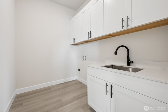 laundry area with washer hookup, cabinet space, light wood-style floors, a sink, and baseboards