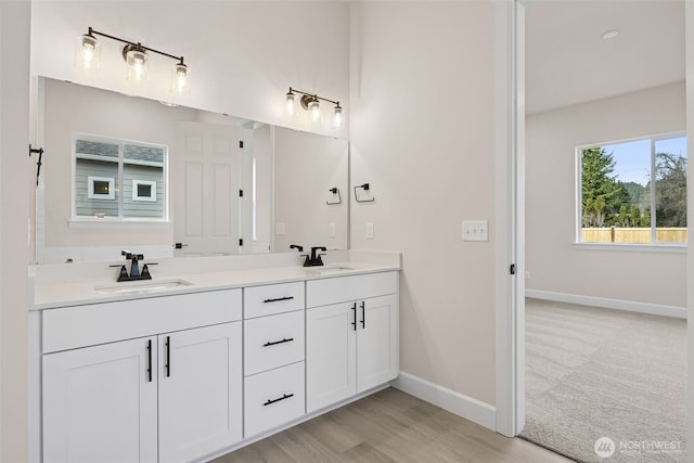 full bath with double vanity, baseboards, a sink, and wood finished floors