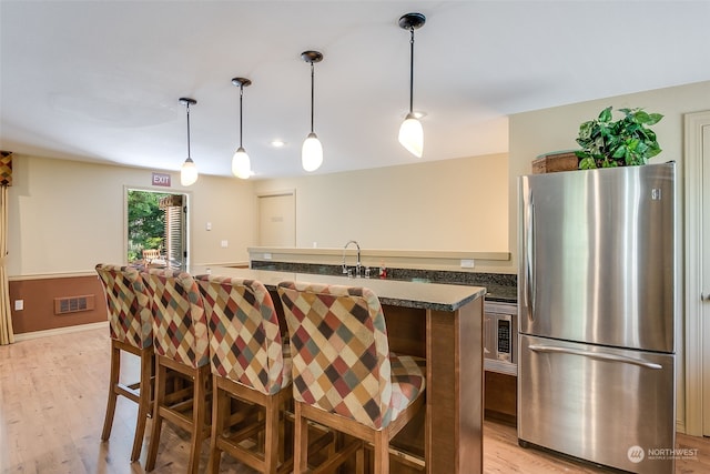 kitchen with pendant lighting, stainless steel refrigerator, a breakfast bar, and light hardwood / wood-style floors