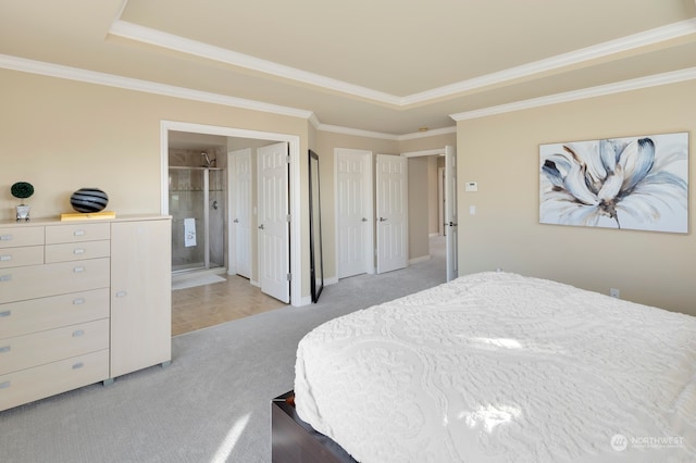 carpeted bedroom with ensuite bathroom, ornamental molding, and a tray ceiling