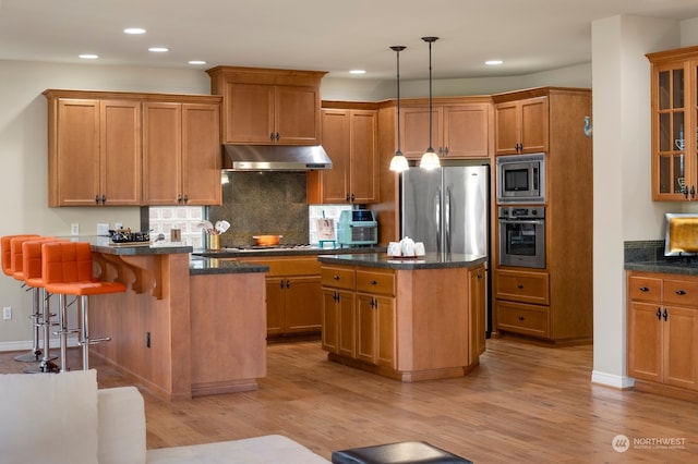 kitchen featuring a kitchen island, appliances with stainless steel finishes, a breakfast bar, light wood-type flooring, and decorative light fixtures