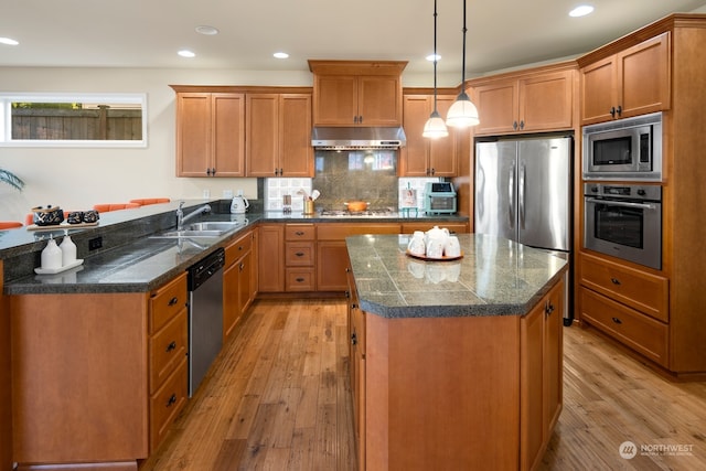 kitchen featuring sink, a kitchen island, stainless steel appliances, pendant lighting, and light hardwood / wood-style flooring