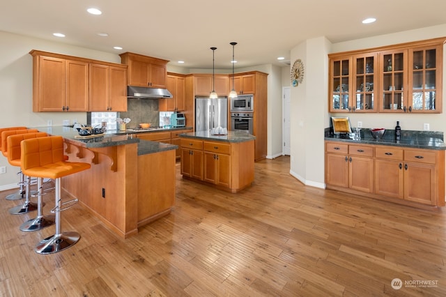 kitchen featuring hanging light fixtures, appliances with stainless steel finishes, a kitchen breakfast bar, light hardwood / wood-style flooring, and a center island