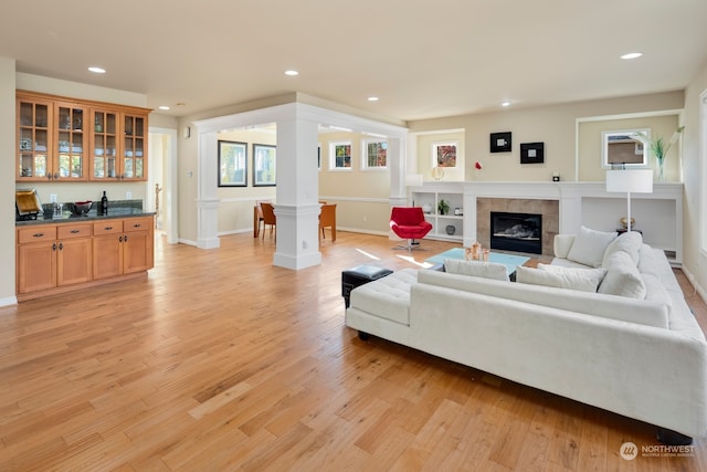 living room with a tiled fireplace, ornate columns, and light hardwood / wood-style flooring