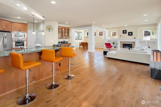 kitchen with a kitchen breakfast bar, stainless steel appliances, decorative columns, pendant lighting, and light hardwood / wood-style floors