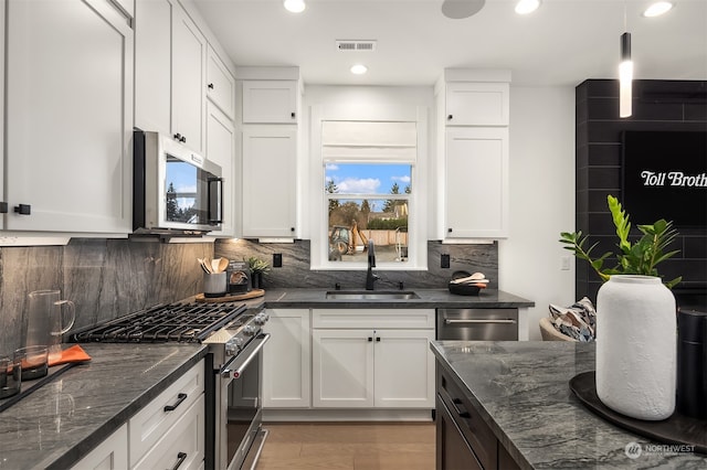 kitchen with stainless steel appliances, white cabinetry, and dark stone countertops