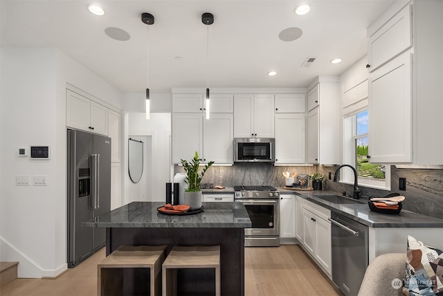 kitchen with stainless steel appliances, sink, white cabinets, a kitchen island, and hanging light fixtures