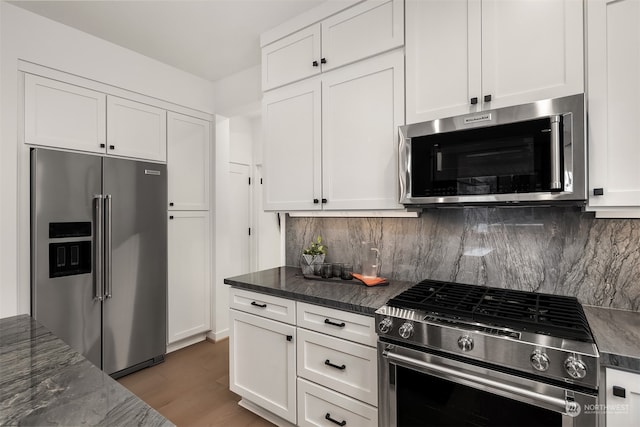 kitchen with tasteful backsplash, premium appliances, dark stone countertops, dark hardwood / wood-style floors, and white cabinetry