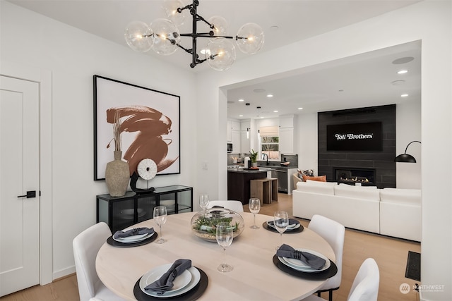 dining area featuring sink, a large fireplace, an inviting chandelier, and light hardwood / wood-style flooring