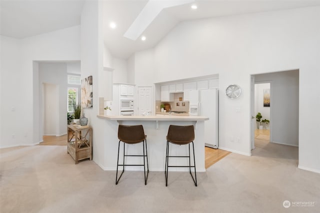 kitchen featuring kitchen peninsula, a kitchen bar, light colored carpet, white cabinets, and white appliances