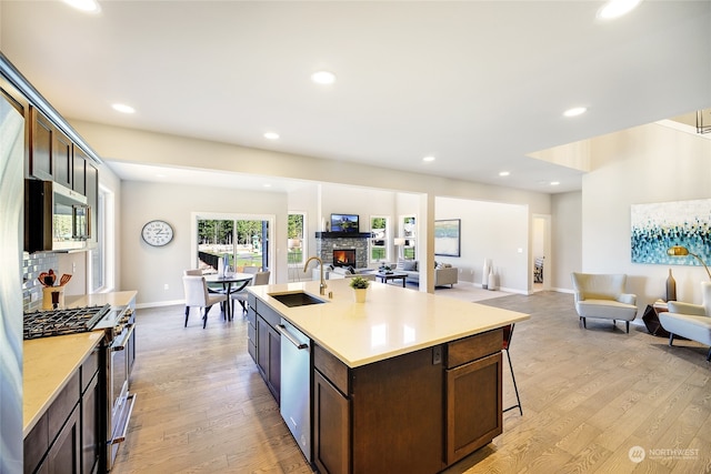 kitchen featuring a center island with sink, light wood-type flooring, sink, dark brown cabinetry, and stainless steel appliances