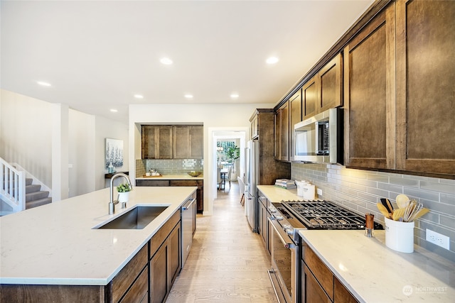 kitchen featuring tasteful backsplash, light stone countertops, sink, light wood-type flooring, and stainless steel appliances