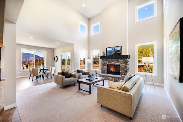 living room with a stone fireplace, light hardwood / wood-style flooring, a high ceiling, and a wealth of natural light