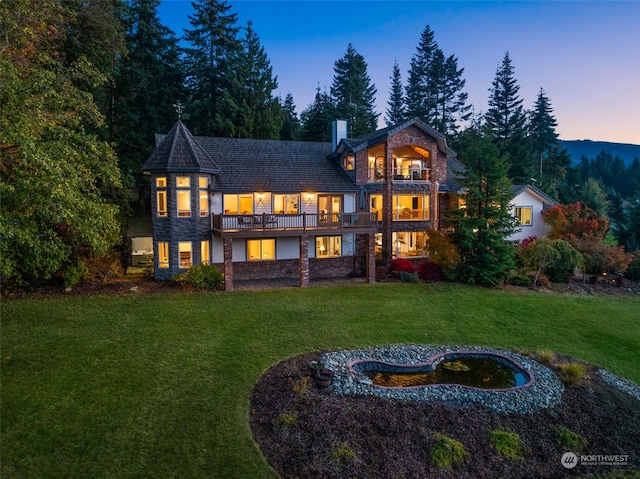 back house at dusk featuring a lawn and a balcony