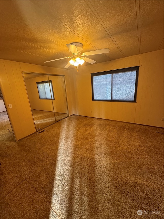 spare room featuring ceiling fan, wood walls, a textured ceiling, and carpet flooring