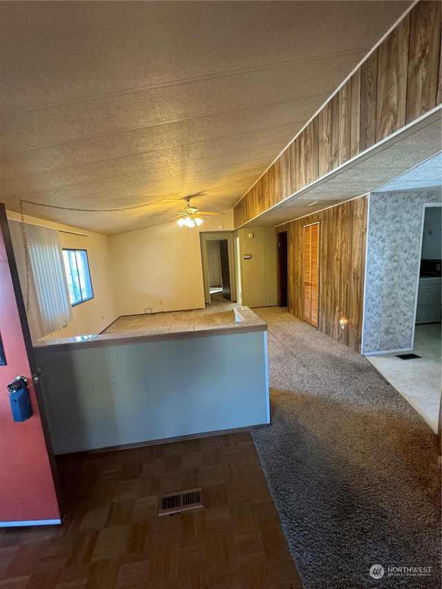 unfurnished room featuring ceiling fan, dark parquet floors, a textured ceiling, and wooden walls