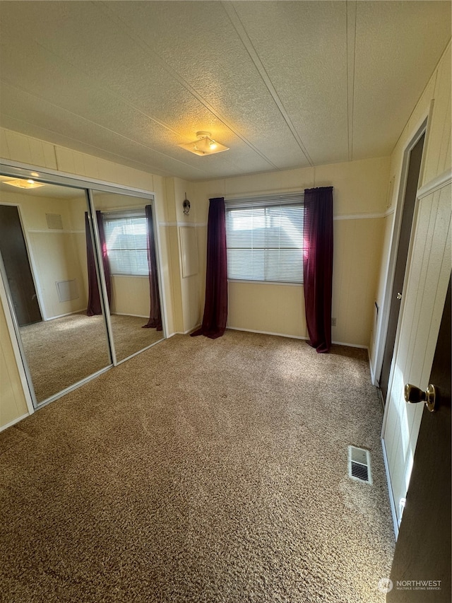 unfurnished bedroom featuring carpet, a textured ceiling, multiple windows, and a closet