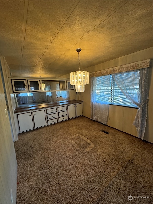 kitchen with a textured ceiling, dark colored carpet, and decorative light fixtures