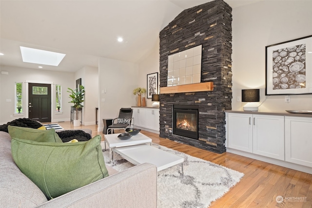 living room featuring a fireplace, light hardwood / wood-style flooring, and vaulted ceiling with skylight