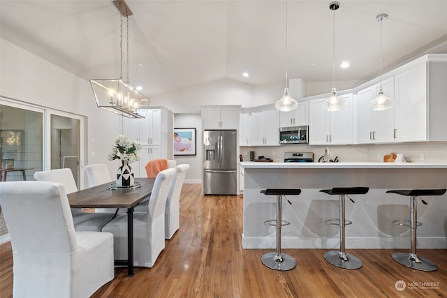 kitchen featuring stainless steel appliances, pendant lighting, light hardwood / wood-style floors, white cabinets, and lofted ceiling