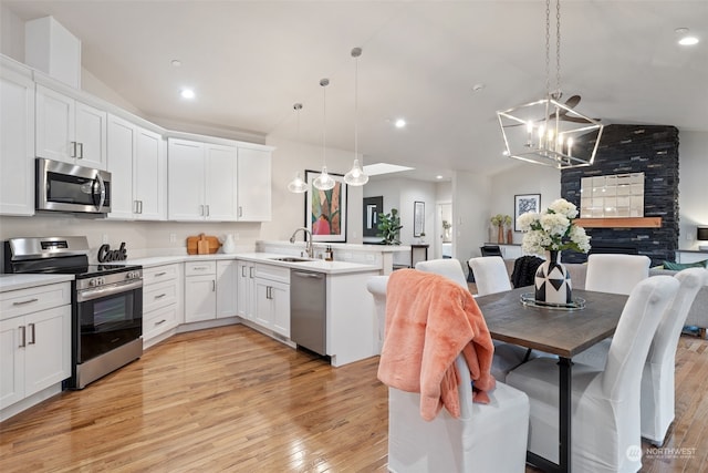 kitchen featuring light wood-type flooring, appliances with stainless steel finishes, lofted ceiling, and decorative light fixtures