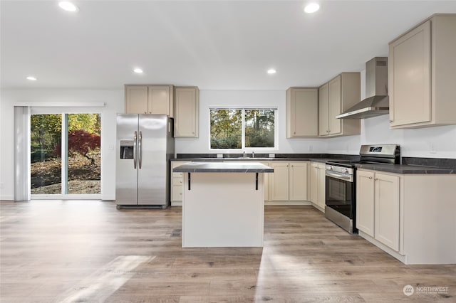 kitchen with a kitchen island, wall chimney range hood, cream cabinetry, light wood-type flooring, and appliances with stainless steel finishes