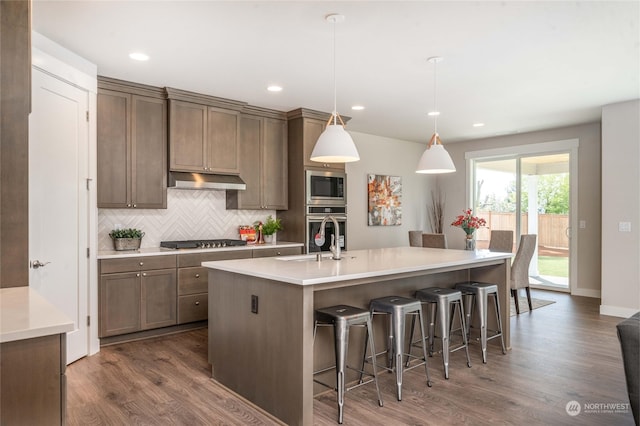 kitchen featuring an island with sink, stainless steel appliances, dark wood-type flooring, sink, and decorative light fixtures