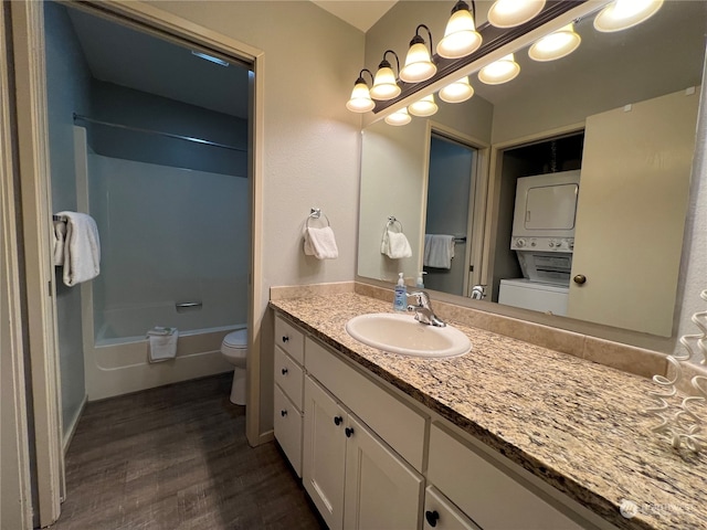 full bathroom featuring  shower combination, stacked washer / dryer, hardwood / wood-style floors, toilet, and vanity