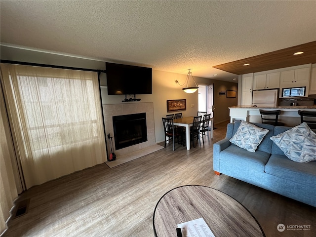 living room featuring a tile fireplace, a textured ceiling, and light hardwood / wood-style floors