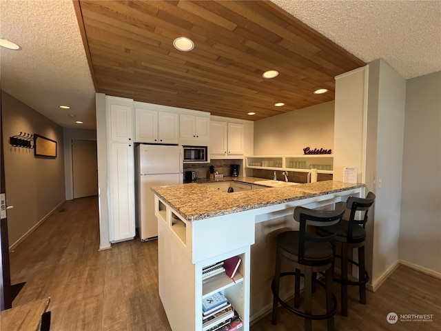 kitchen with kitchen peninsula, built in microwave, white cabinetry, white fridge, and dark hardwood / wood-style floors