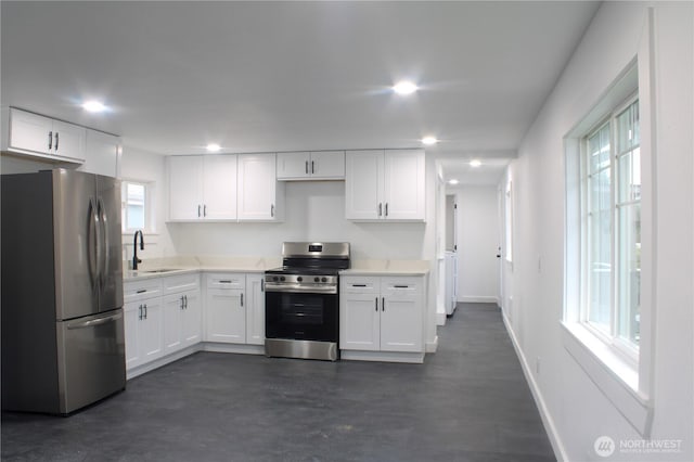 kitchen featuring light countertops, appliances with stainless steel finishes, white cabinetry, a sink, and baseboards