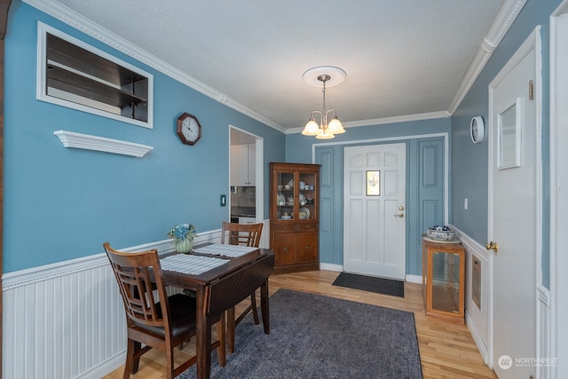 dining area with a textured ceiling, a notable chandelier, crown molding, and light hardwood / wood-style flooring