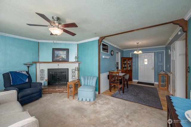 living room featuring ceiling fan with notable chandelier, a textured ceiling, a fireplace, wood-type flooring, and crown molding