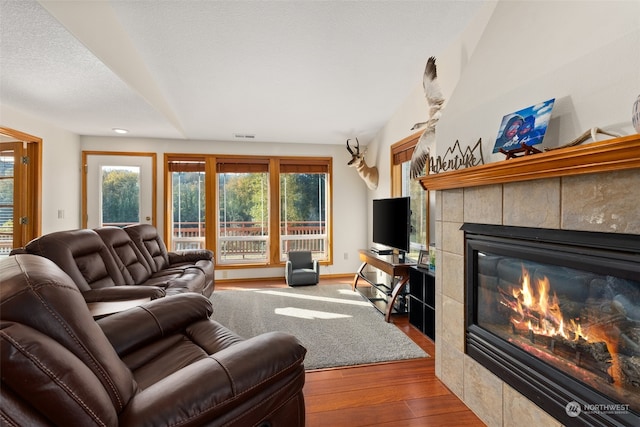 living room with a textured ceiling, hardwood / wood-style flooring, and a tiled fireplace