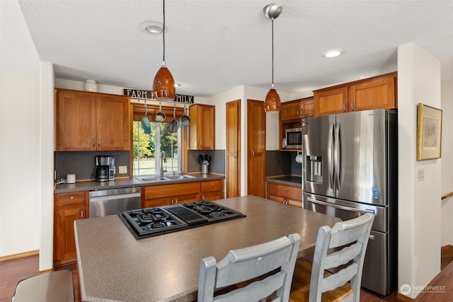 kitchen featuring dark hardwood / wood-style floors, stainless steel appliances, sink, a center island, and pendant lighting