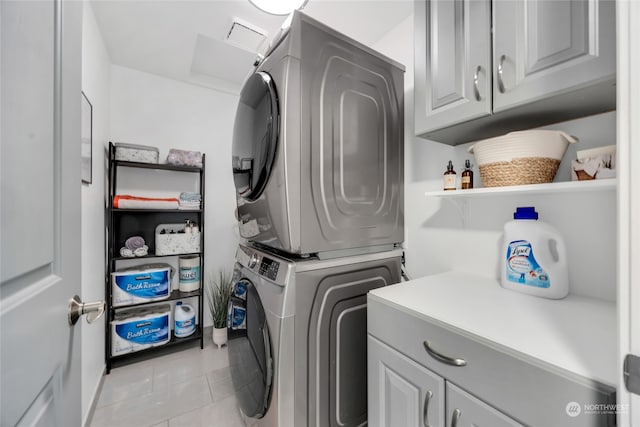 laundry room with stacked washer and dryer, light tile patterned floors, and cabinets