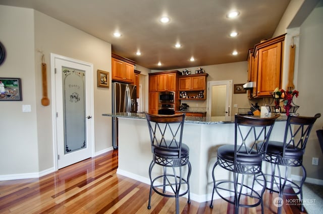 kitchen with dark stone counters, light hardwood / wood-style floors, a kitchen breakfast bar, and stainless steel appliances