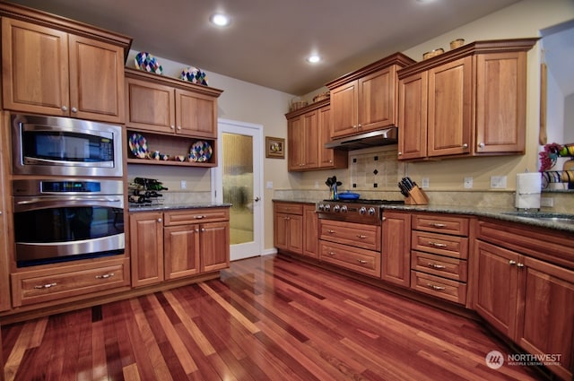 kitchen featuring dark wood-type flooring, dark stone countertops, backsplash, and appliances with stainless steel finishes