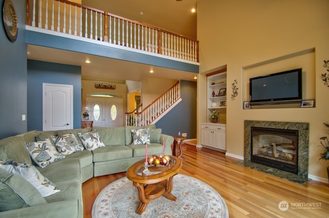 living room featuring built in shelves, a towering ceiling, hardwood / wood-style flooring, and a premium fireplace