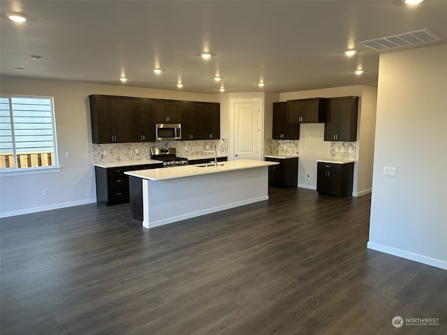 kitchen with a center island with sink, sink, appliances with stainless steel finishes, dark hardwood / wood-style flooring, and dark brown cabinetry