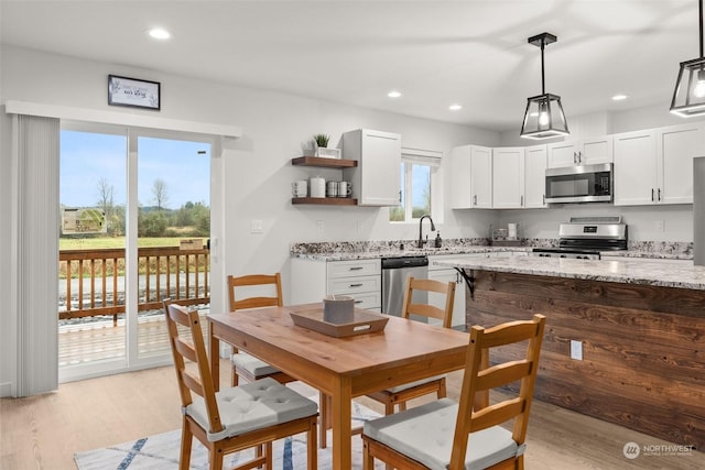 kitchen with white cabinetry, light stone counters, decorative light fixtures, appliances with stainless steel finishes, and light wood-type flooring