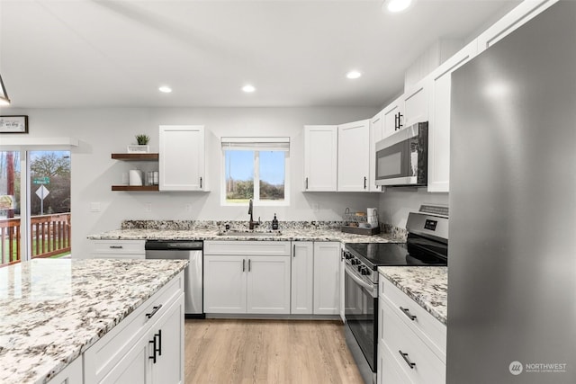 kitchen with white cabinetry, sink, light stone counters, appliances with stainless steel finishes, and light wood-type flooring