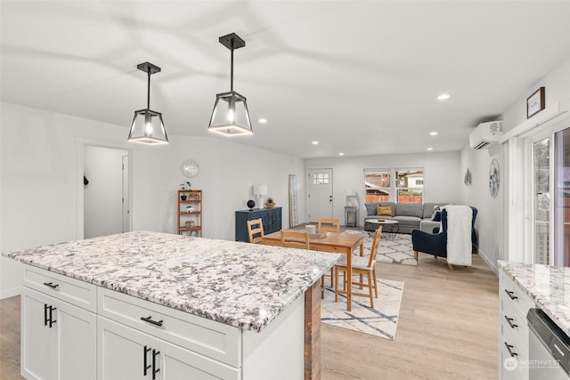 kitchen featuring a wall unit AC, white cabinets, hanging light fixtures, and light wood-type flooring