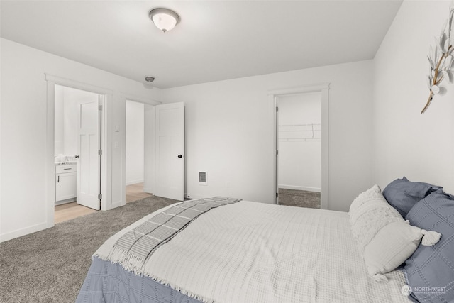 bedroom with ensuite bathroom, light colored carpet, a walk in closet, and a closet