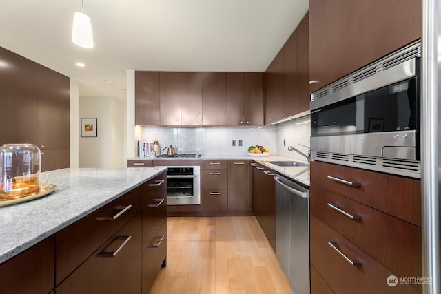 kitchen with stainless steel appliances, backsplash, sink, pendant lighting, and light wood-type flooring